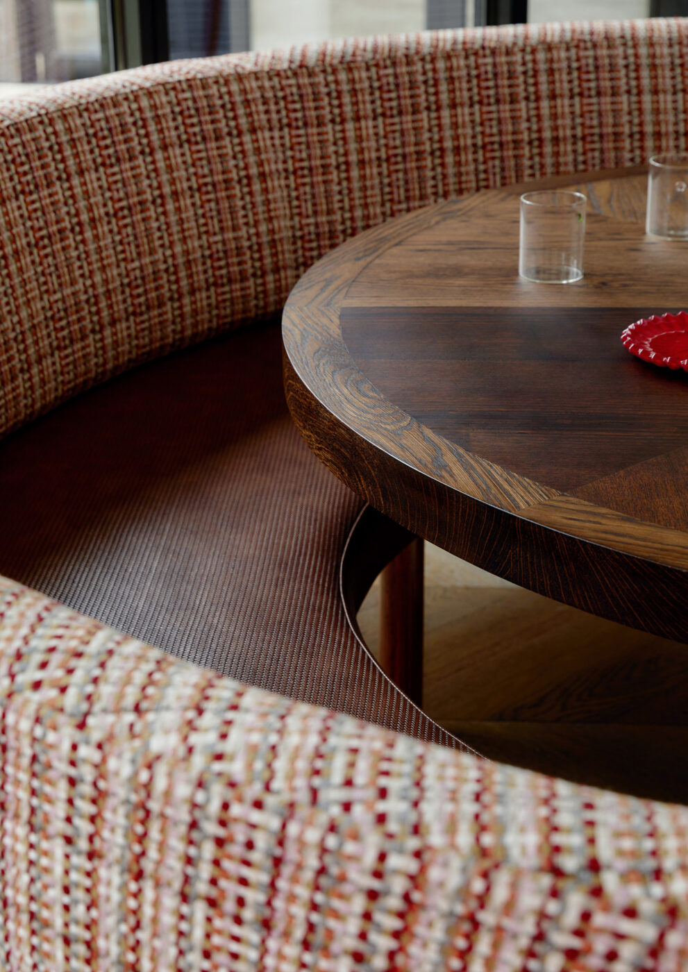 Designer breakfast nook detail with a leather like strap banquette seat, woven fabric fixed back cushions and a custom table featuring an inset decorative pattern, combining luxurious materials and bespoke joinery.