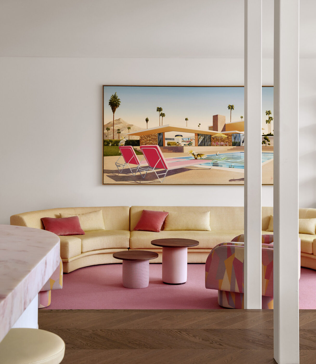 Elegant contemporary living room with a soft yellow modular sofa, blush pink goat hair rug, swivel chairs upholstered in graphic fabric and a large-scale artwork inspired by glamorous 1950s poolside photography.