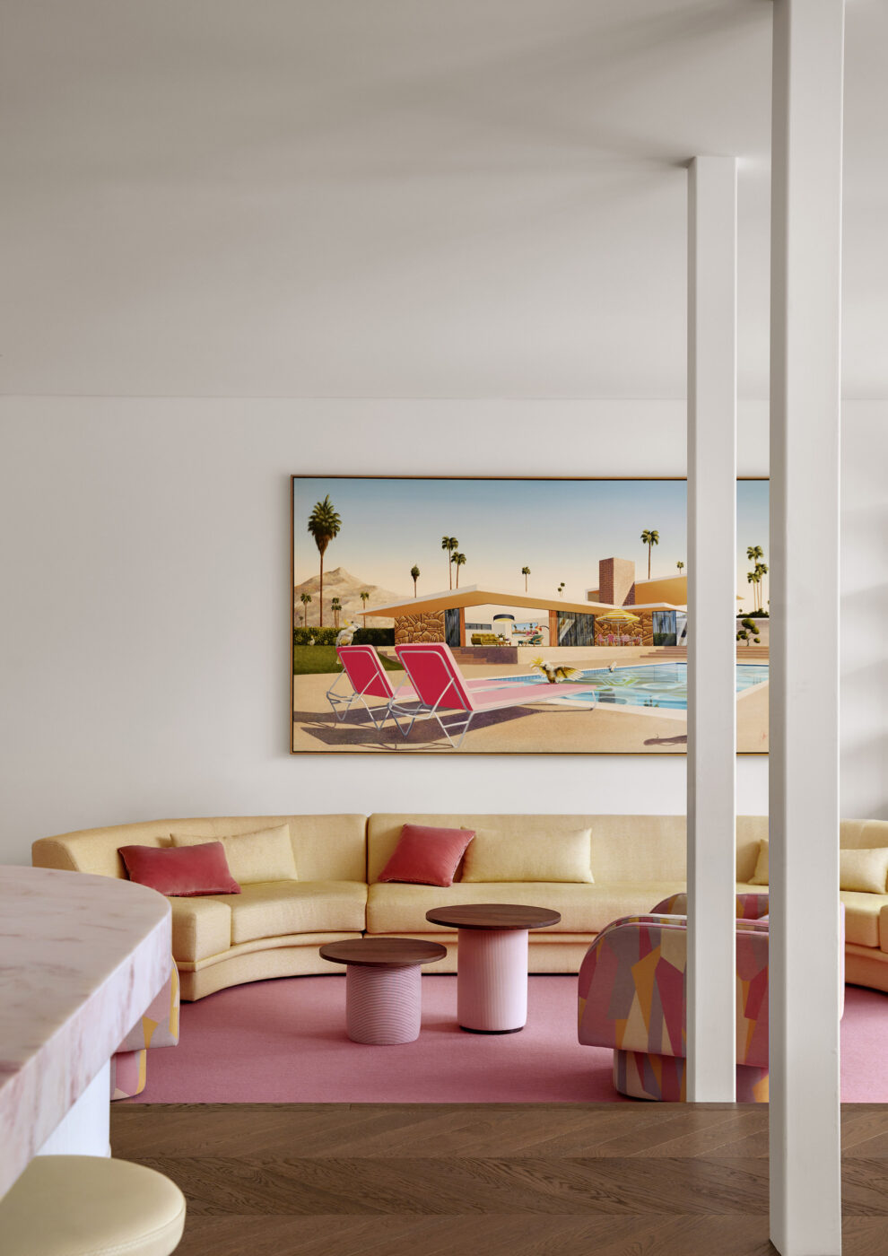 Elegant contemporary living room with a soft yellow modular sofa, blush pink goat hair rug, swivel chairs upholstered in graphic fabric and a large-scale artwork inspired by glamorous 1950s poolside photography.