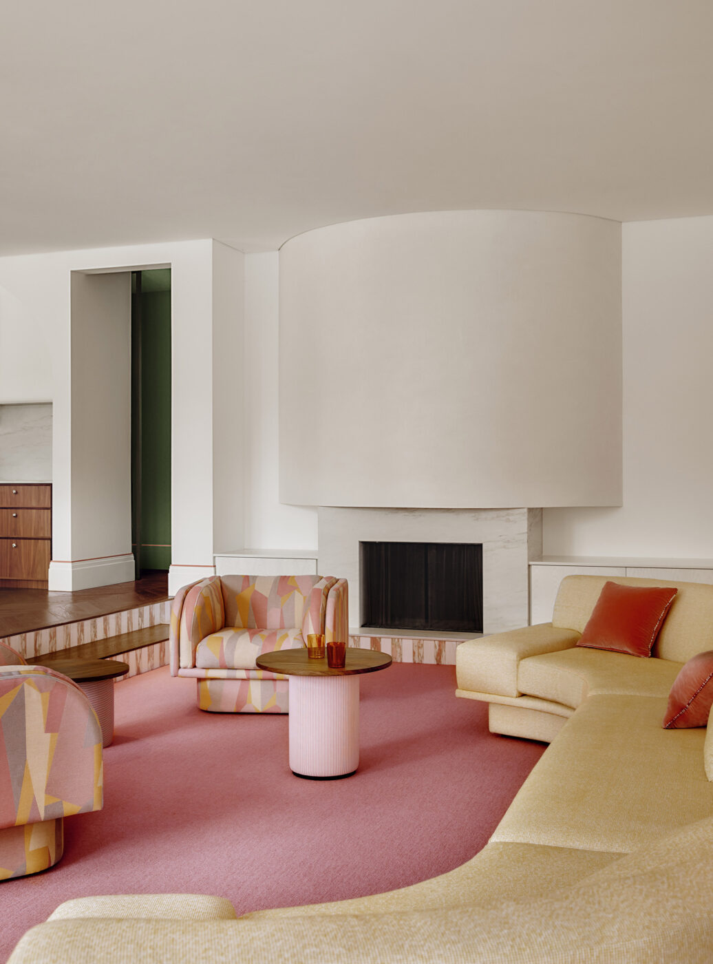 Luxury family living room located in Brighton, showcasing a pink goat hair carpet, curved plaster fireplace, large modular sofa in soft yellow upholstery and graphic fabric swivel chairs, creating a vibrant and comfortable contemporary interior.