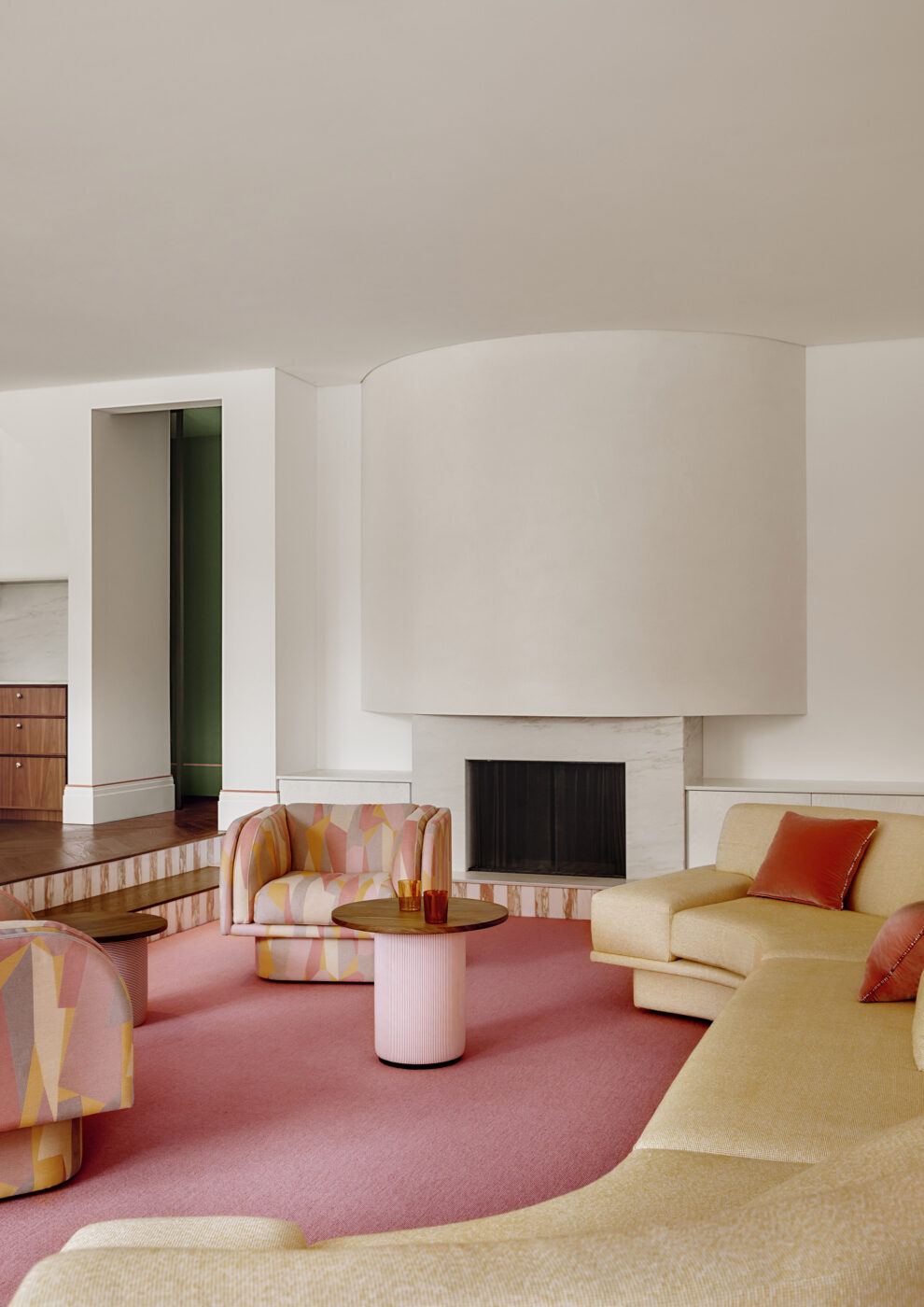 Luxury family living room showcasing a pink goat hair carpet, curved plaster fireplace, large modular sofa in soft yellow upholstery and graphic fabric swivel chairs, creating a vibrant and comfortable contemporary interior.