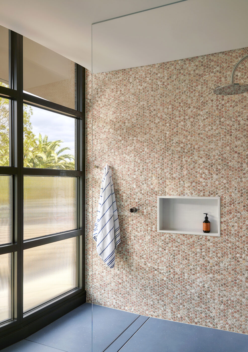 Designer walk-in shower with pink and white penny mosaic wall tiles, oversized blue floor tiles and contemporary detailing, blending colour, pattern and texture in a luxurious ensuite bathroom.