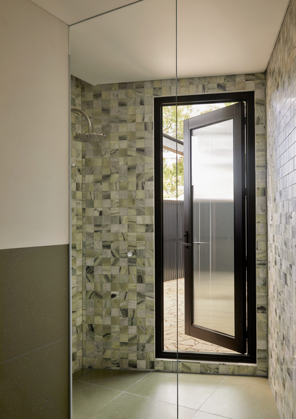 Designer ensuite bathroom showcasing a shower lined with green and white marble tiles, matching green flooring and a door leading to a private balcony, creating a fresh and sophisticated indoor-outdoor retreat.