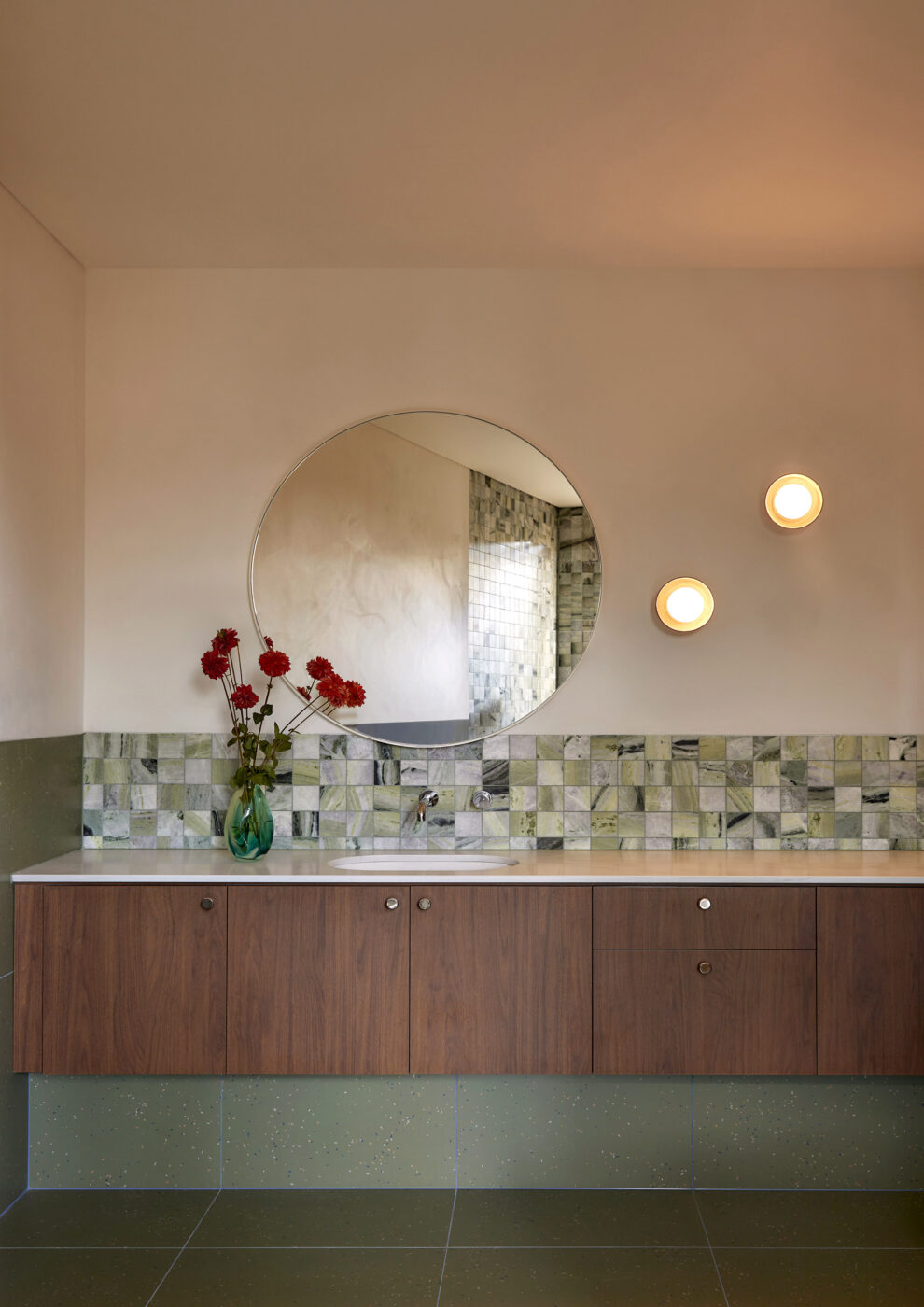 Luxury bathroom showcasing a bespoke timber vanity, green and white marble tiles, textured limewashed walls, oversized circular mirror and porcelain wall lighting, creating a refined and inviting contemporary interior.