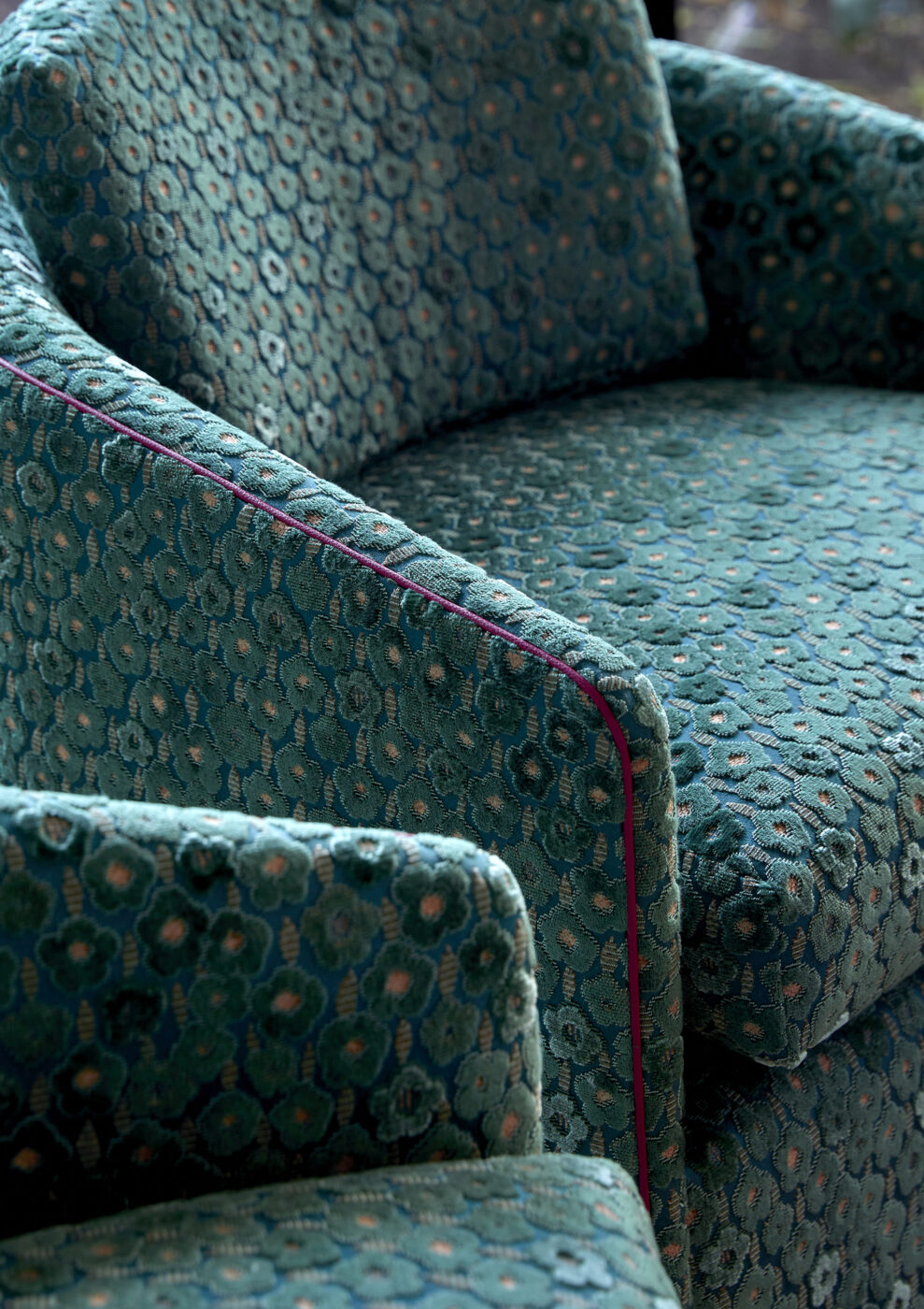 Designer furniture detail featuring a bespoke chair upholstered in green floral velvet with contrasting pink leather piping, highlighting custom upholstery, artisanal craftsmanship and rich material layering.