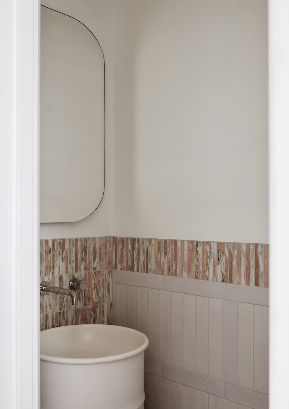 Designer powder room with a white steel pedestal sink, wall-mounted tapware and a statement row of pink and white marble finger tiles, creating a sophisticated space with clean white walls and timeless detailing.